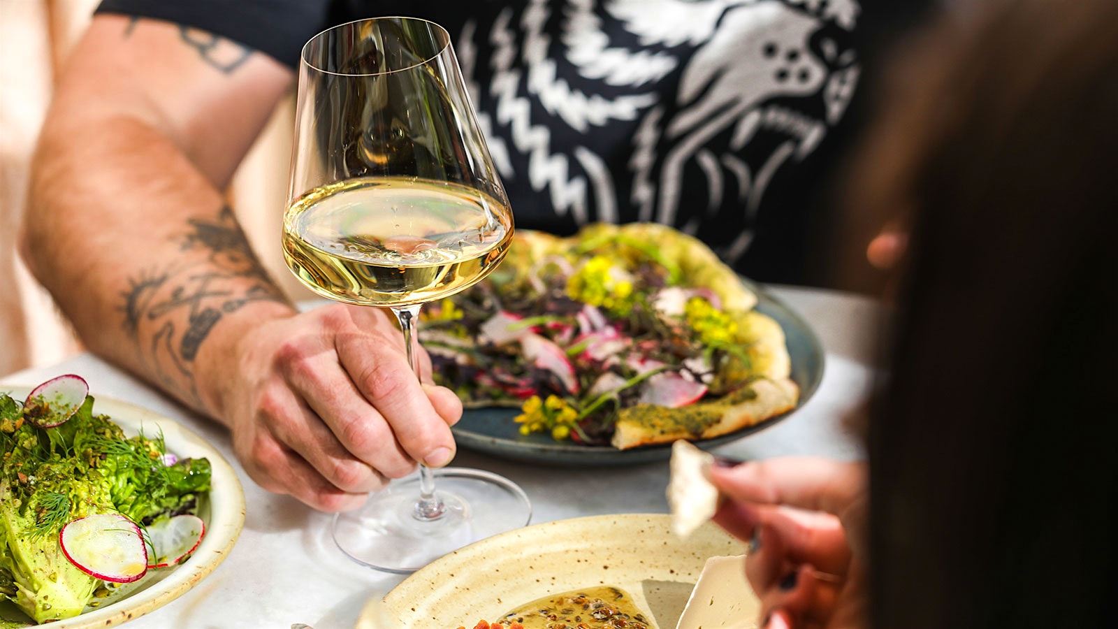 Two people dining at Little Saint, with plates of sun-dried tomatoes, flatbread, vegetables and flowers